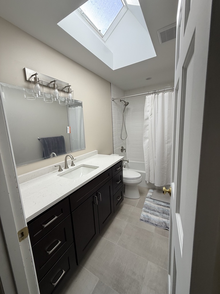 Dark vanity, light tile, and skylight